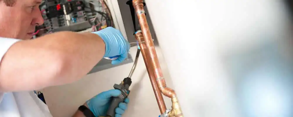 Water heater repair technician testing copper pipe connections and controls in Boulder, CO